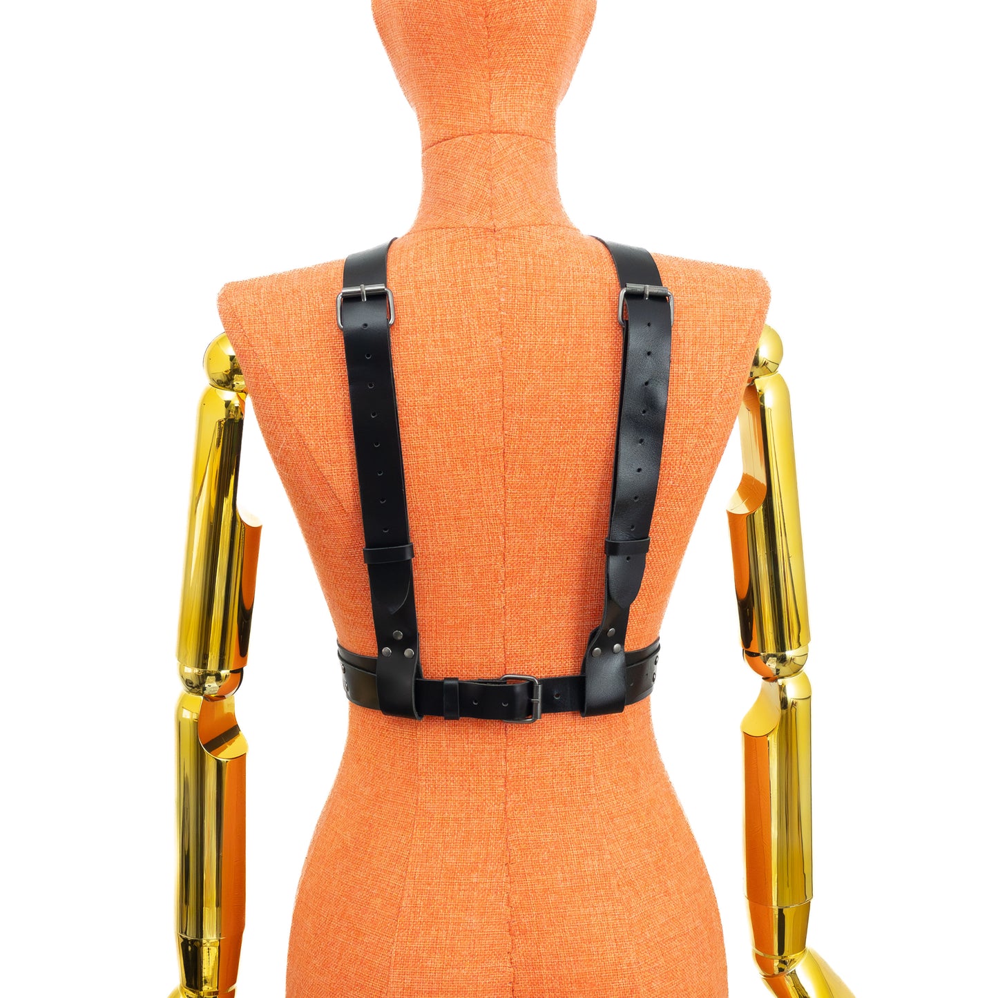 Three-quarter front view of black leather reversible chest harness worn on a mannequin in single strap front configuration, showing central vertical strap, adjustable buckles on shoulder straps, and layered waist belt with dark nickel hardware.