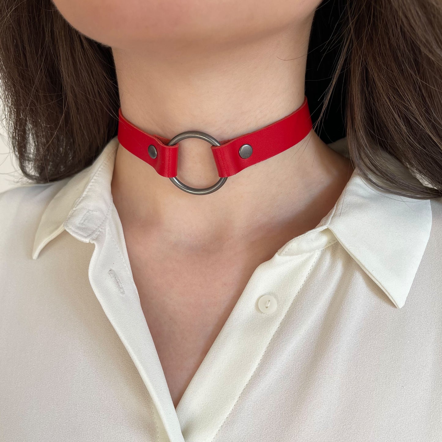 Red leather choker with black ring – angled front view on model with ivory shirt.
