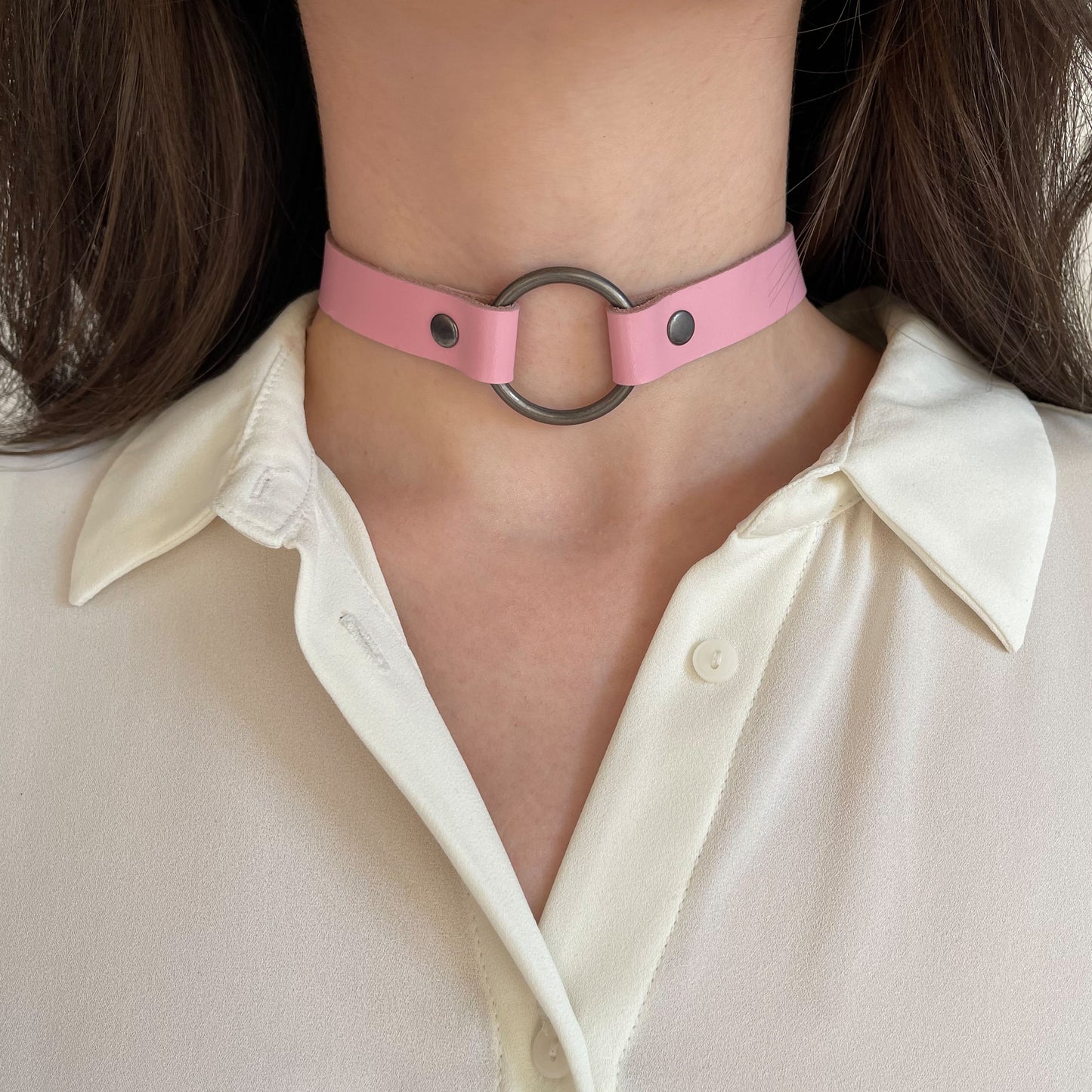 Pink leather choker with dark O-ring – centered front view on white blouse.