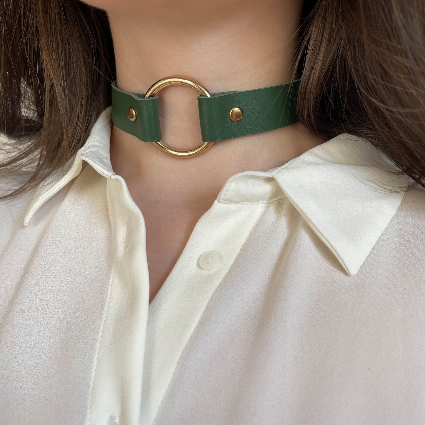 Close-up of green leather choker with gold O-ring and rivets, worn over white blouse, angled view
