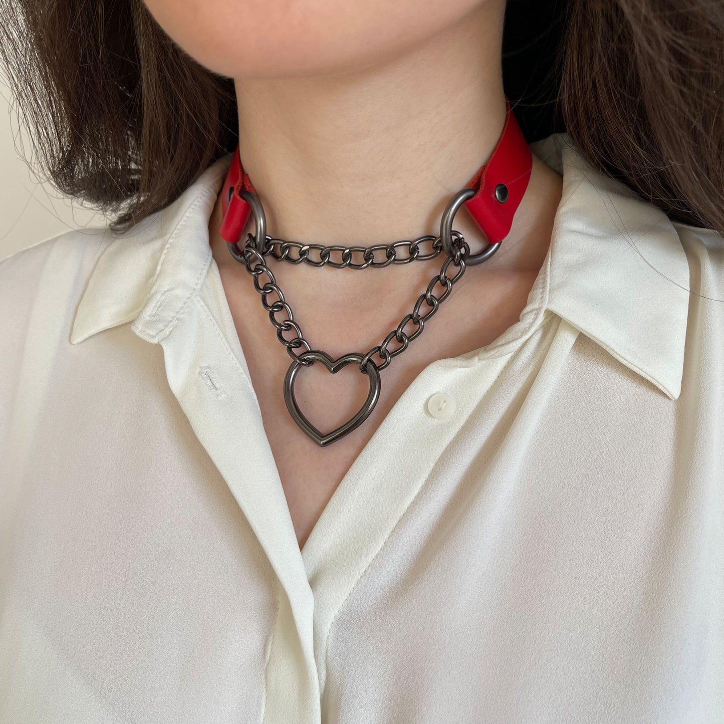 Red leather choker with dark metal heart-shaped hardware on model’s neck, side view