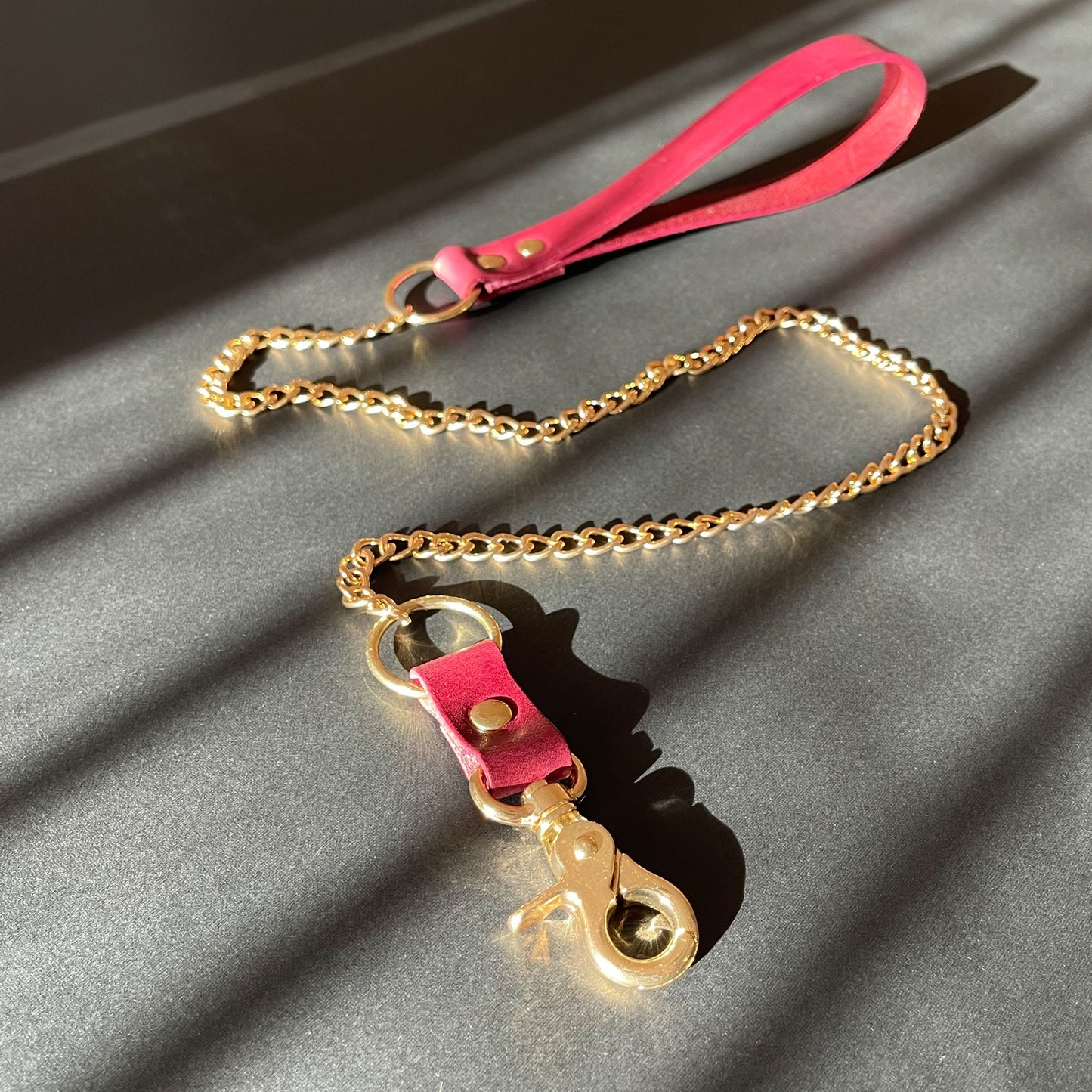 Gold chain bondage leash with marsala leather handle on a gray surface
