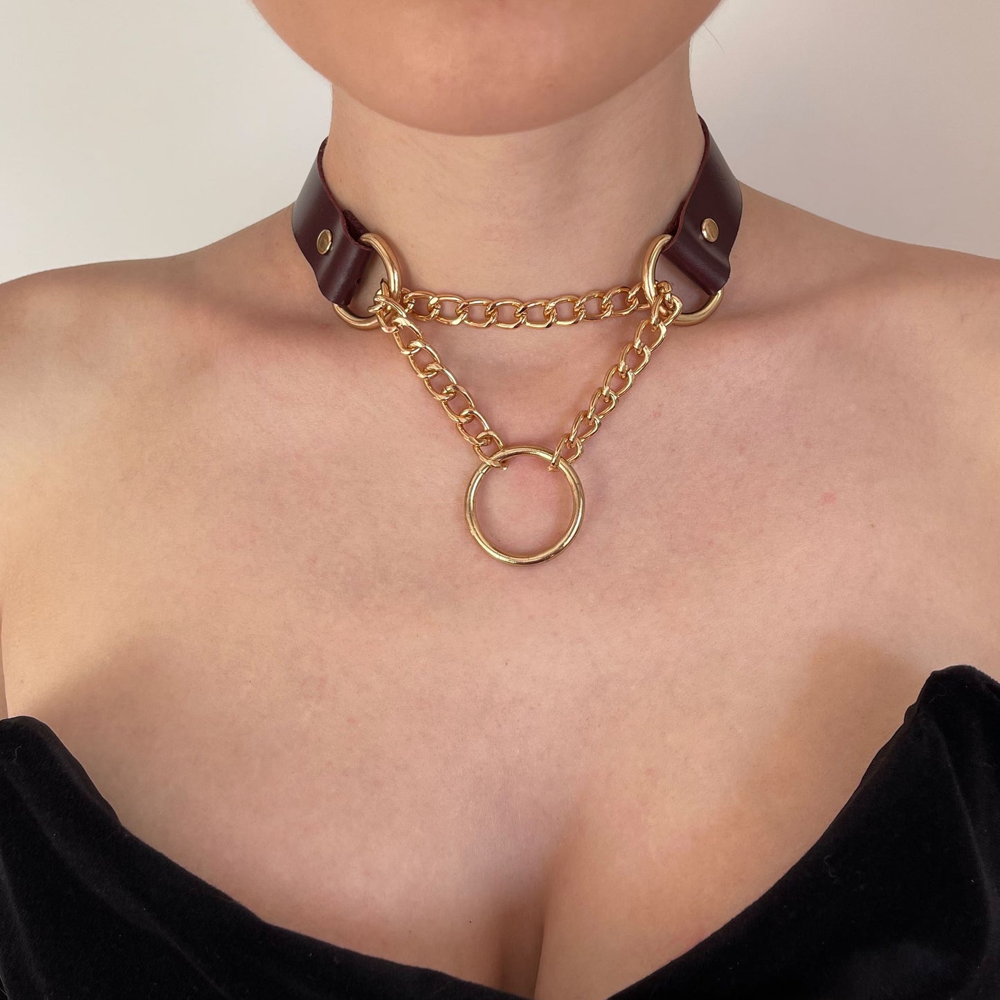 Front view of a marsala leather choker with gold chains and center O-ring. Styled with a black top and silver earrings.