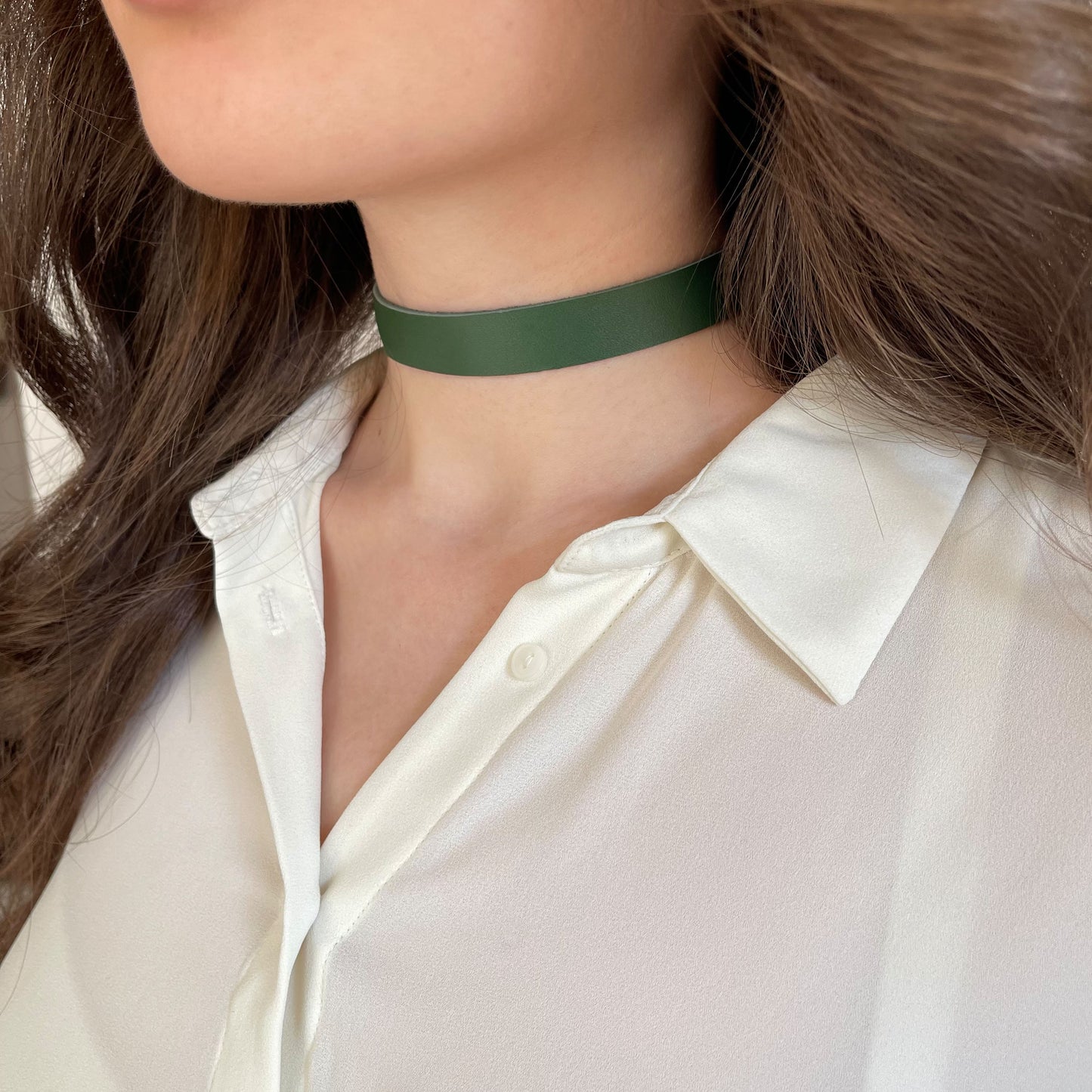 Minimalist green leather choker made from genuine semi-matte leather (1.4–1.8 mm thick), 1.5 cm (0.59 in) wide. Secured with a metal buckle. The photo shows a close-up of a woman’s neck in a white shirt, highlighting the deep green tone. A refined everyday accessory in a clean, modern style.
