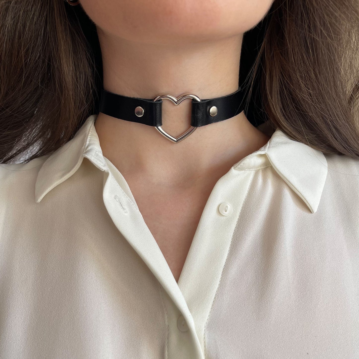 Black leather choker with silver heart-shaped ring – centered front view on model wearing ivory shirt