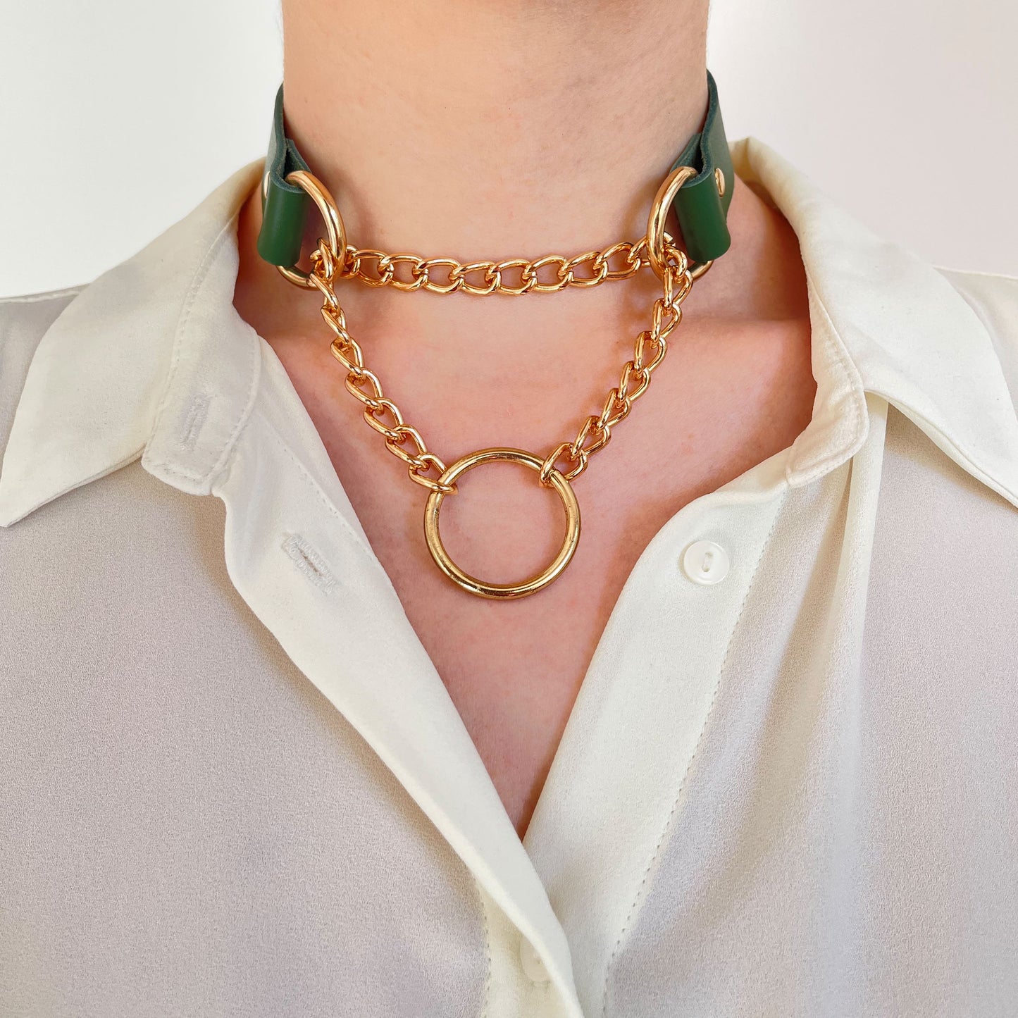 Front view of green leather choker with gold-tone chains and O-ring, styled with a buttoned shirt.
