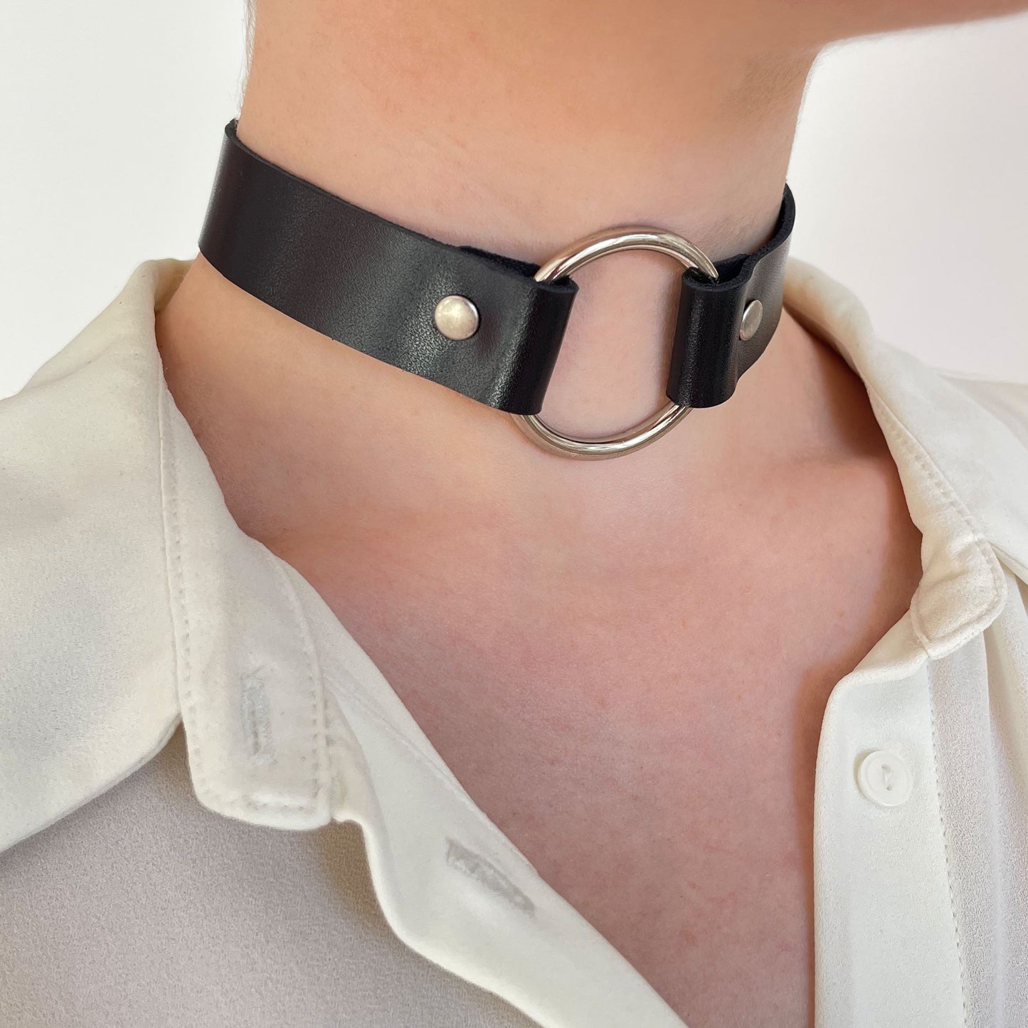 Angled shot of black leather choker with bright silver O-ring, styled on bare neckline