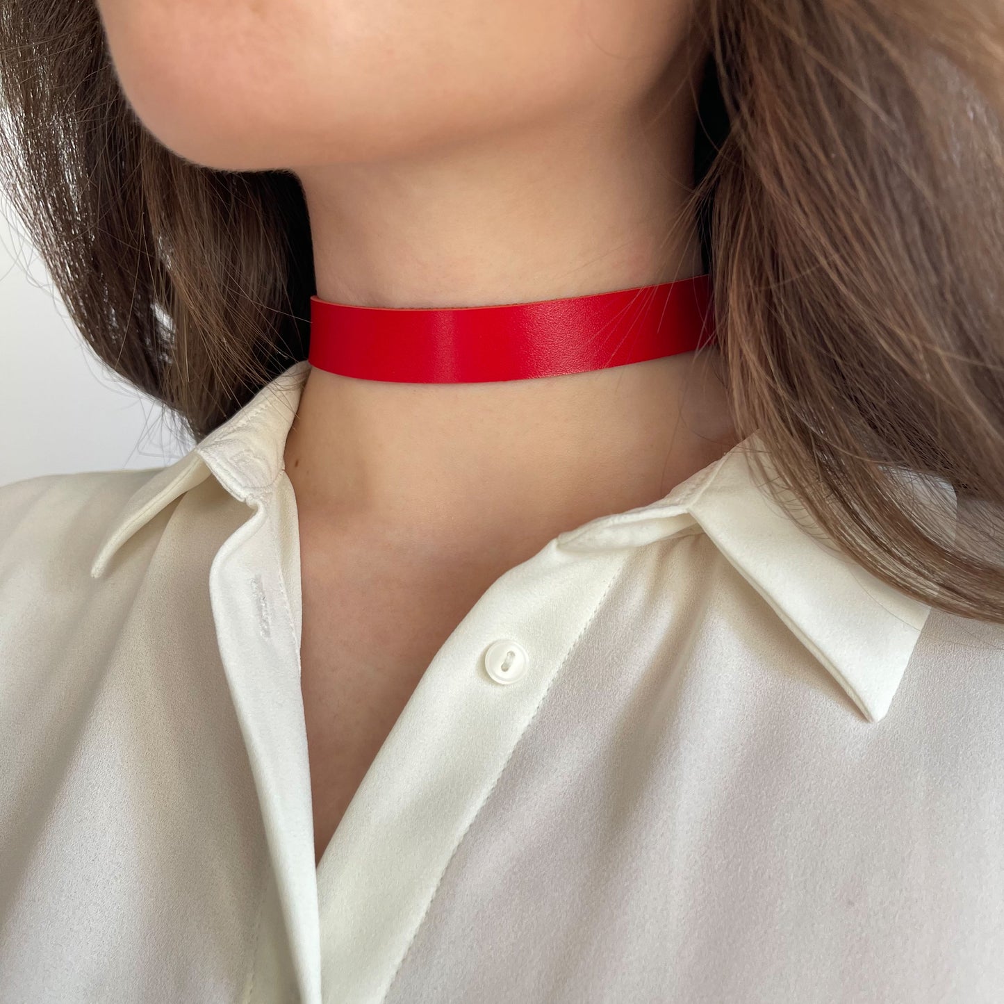 Bold red leather choker made from semi-matte genuine leather (1.4–1.8 mm thick), 1.5 cm (0.59 in) wide, with buckle closure. The vivid color pops against a white shirt, worn by a woman in a close-up. A striking yet wearable accessory, perfect for confident daily looks or bold styling statements.