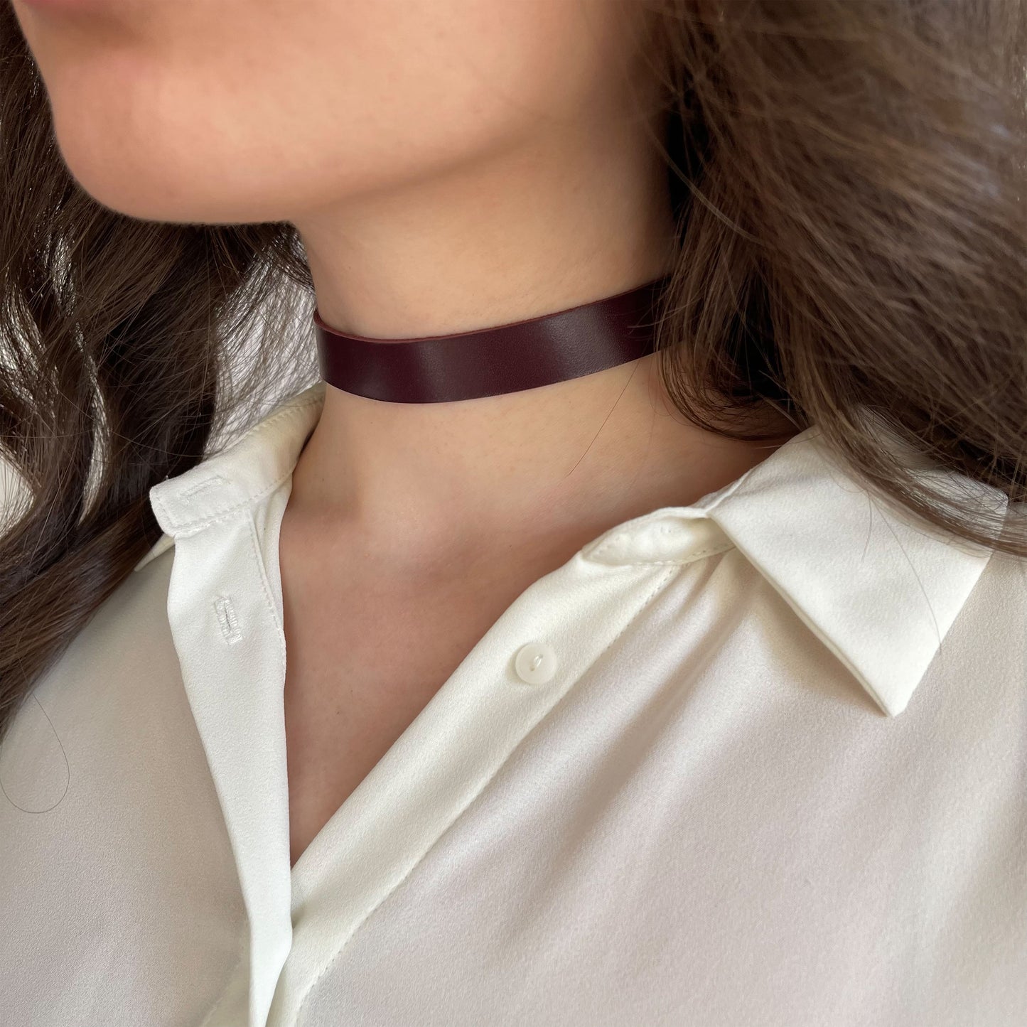 Deep marsala leather choker, 1.5 cm (0.59 in) wide, crafted from genuine semi-matte leather (1.4–1.8 mm thick), secured with a metal buckle. Displayed on a woman's neck in a white shirt, enhancing the richness of the color. Ideal for everyday wear with a subtle sensual edge.