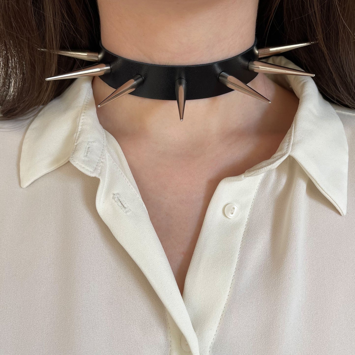 Leather spiked collar worn on the neck, front view, with long silver-colored cone spikes