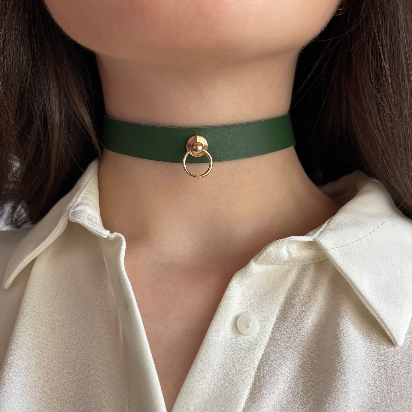 Elegant green leather choker with a central gold-tone ring and rivet. Width: 1.5 cm (0.59 in), made of semi-matte leather (1.4–1.8 mm thick). Worn by a woman in a white shirt, the accessory draws attention to the neck and adds a chic minimalist touch.