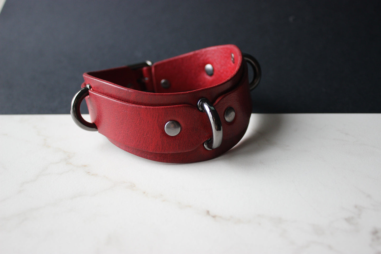 Red leather collar with metal hardware on a white surface and dark background