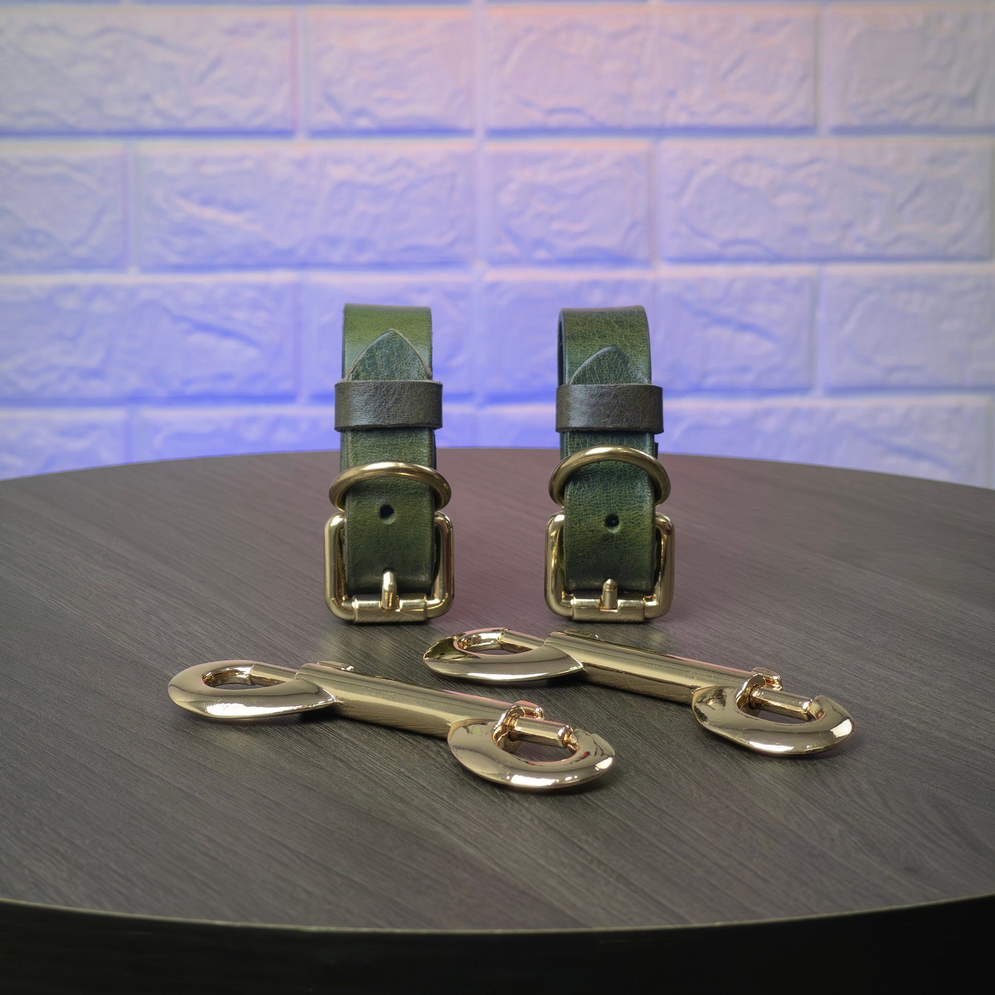 Two green leather straps with gold hardware on a dark surface with a light blue tiled background.