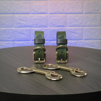 Two green leather straps with gold hardware on a dark surface with a light blue tiled background.