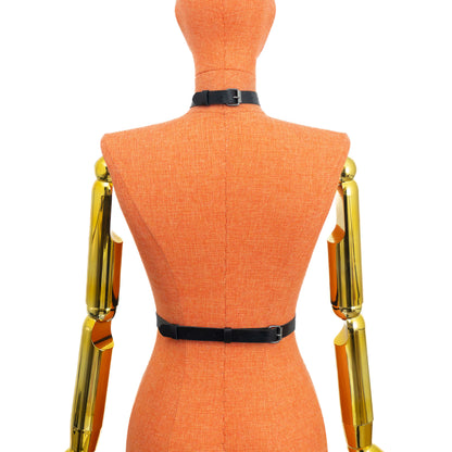 Front view on mannequin of black leather collar harness showing full structure from wide collar to waist, vertical strap connected through round rings, central round ring between the bust, double chains to the waist area, and dark nickel hardware with D-rings located on the straps.
