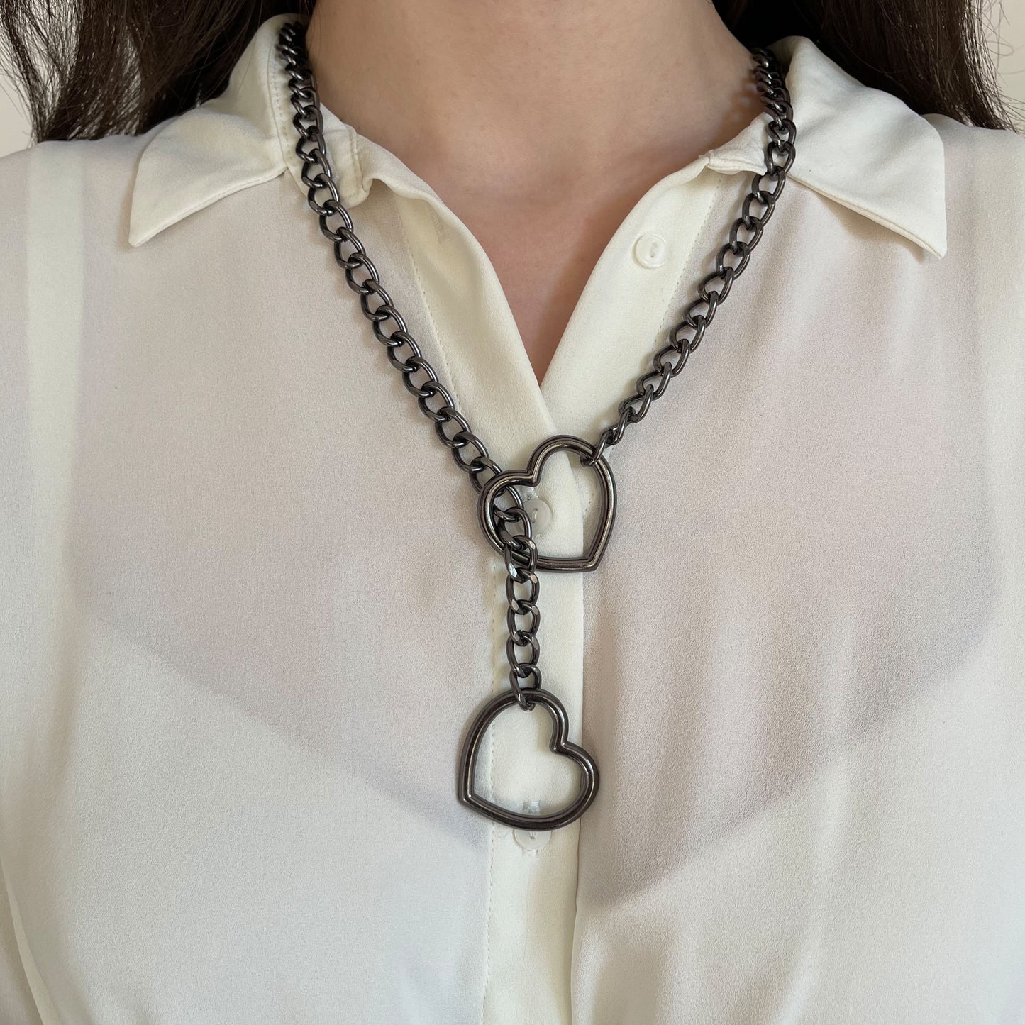 Dark nickel sliding chain collar worn on the neck, heart-shaped ring at the front with chain pulled through, second heart ring hanging vertically, chain resting evenly against the neck, shown from a straight-on angle.
