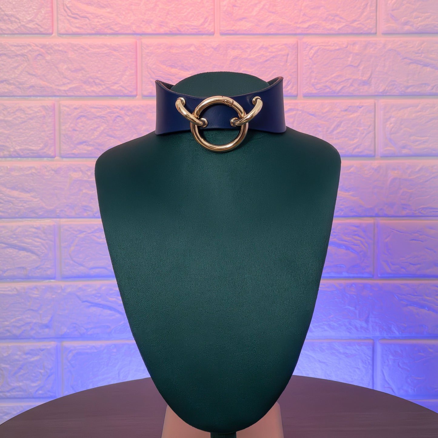 Mannequin head with a blue leather collar featuring a gold ring on a textured purple background