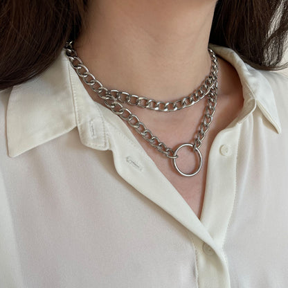 Double chain choker in silver color worn on the neck, semi-side view. Two parallel chains form a layered collar line. The front connection features a round metal ring, while the back of the choker is secured with a lobster clasp.