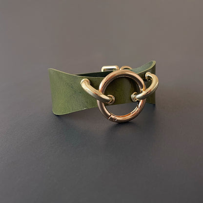 Green leather choker with gold metal hardware on a dark gray background