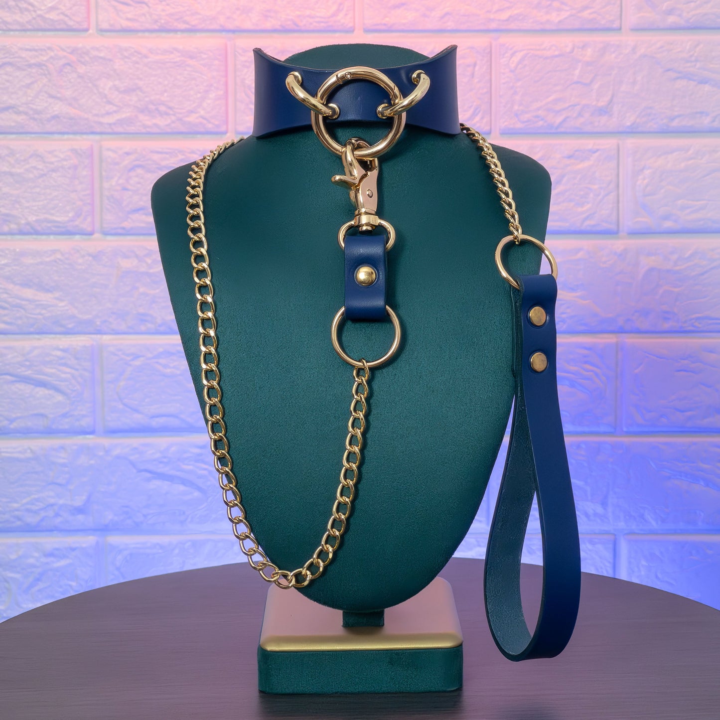 Blue collar with gold chain on a green mannequin against a textured purple wall.