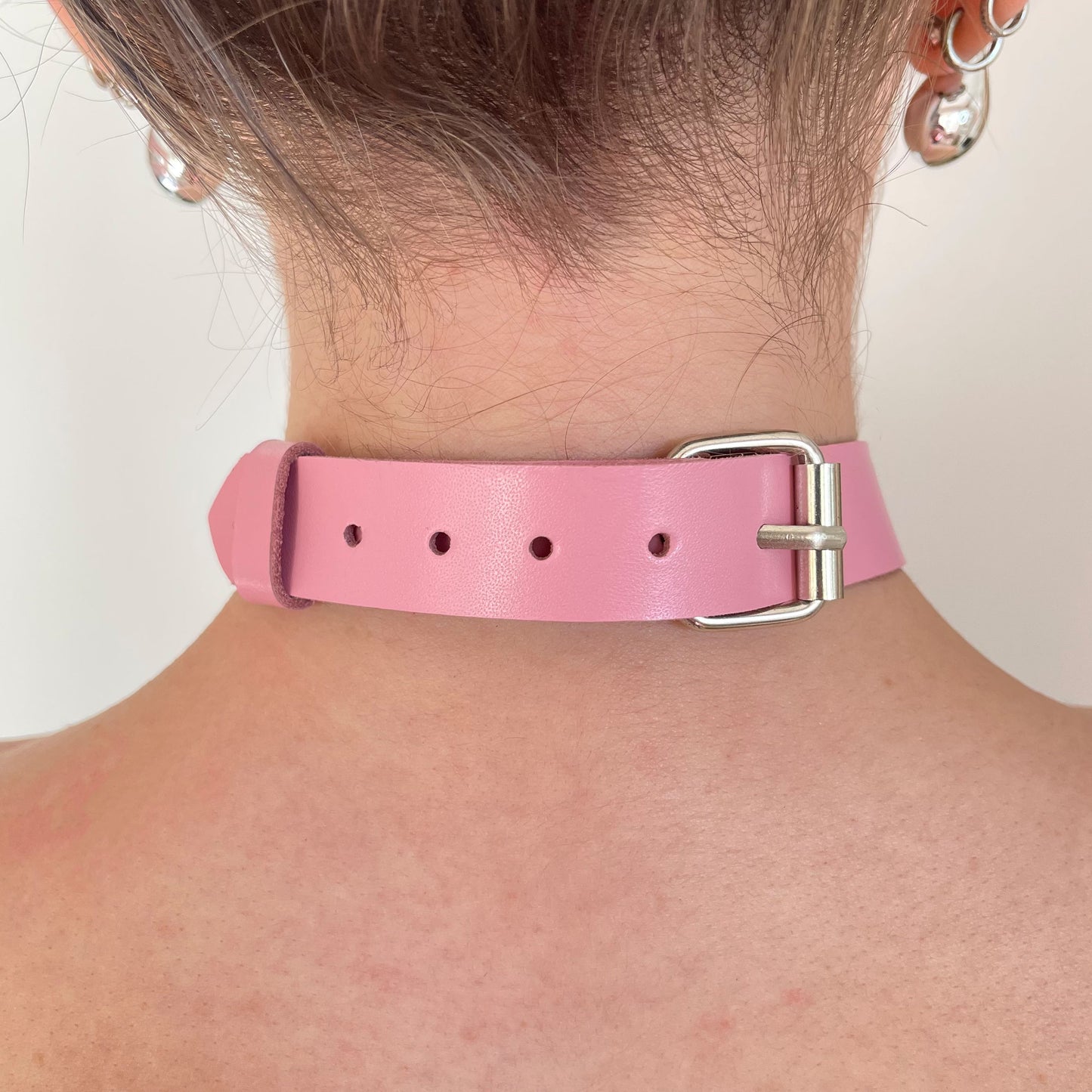 Back view of a pink leather choker showing the silver buckle, adjustment holes, and strap end secured with a keeper, leather lying flat against the neck with a straight cut edge along the strap.