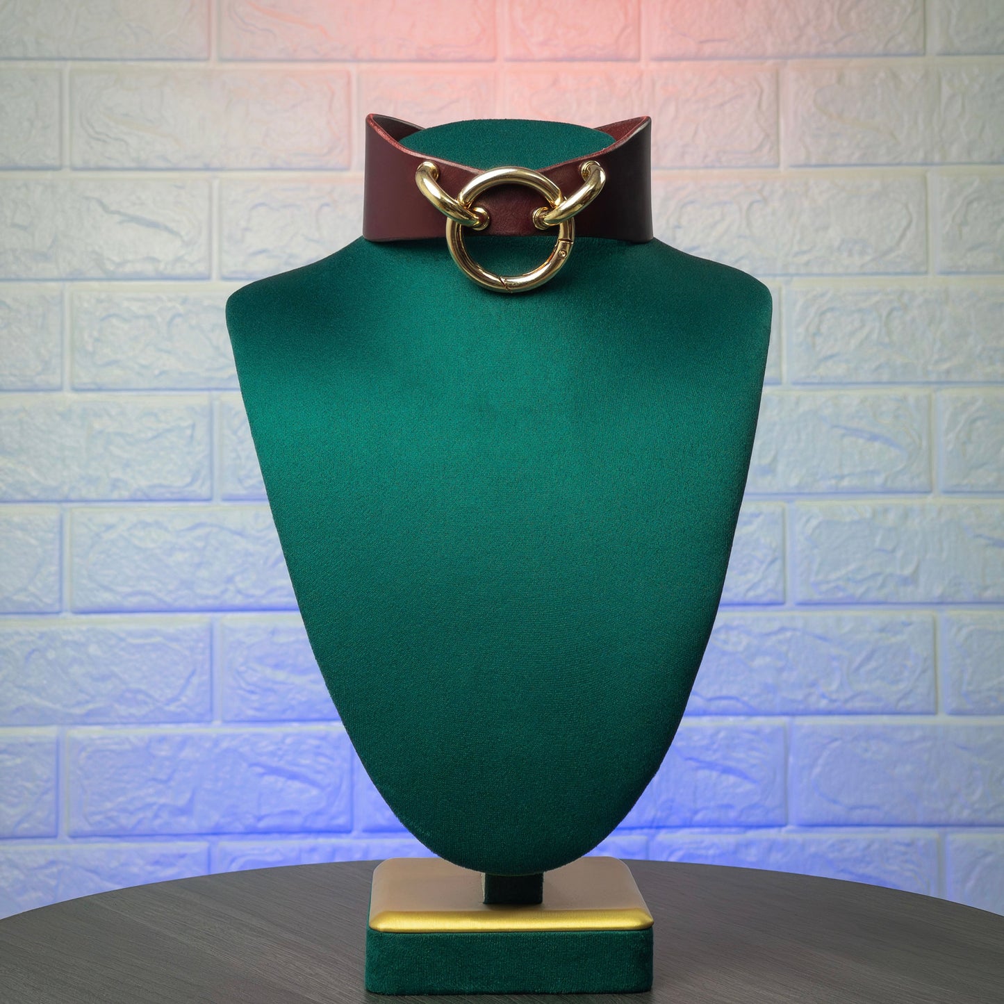 Green mannequin head with a marsala choker with gold hardware on a textured white background