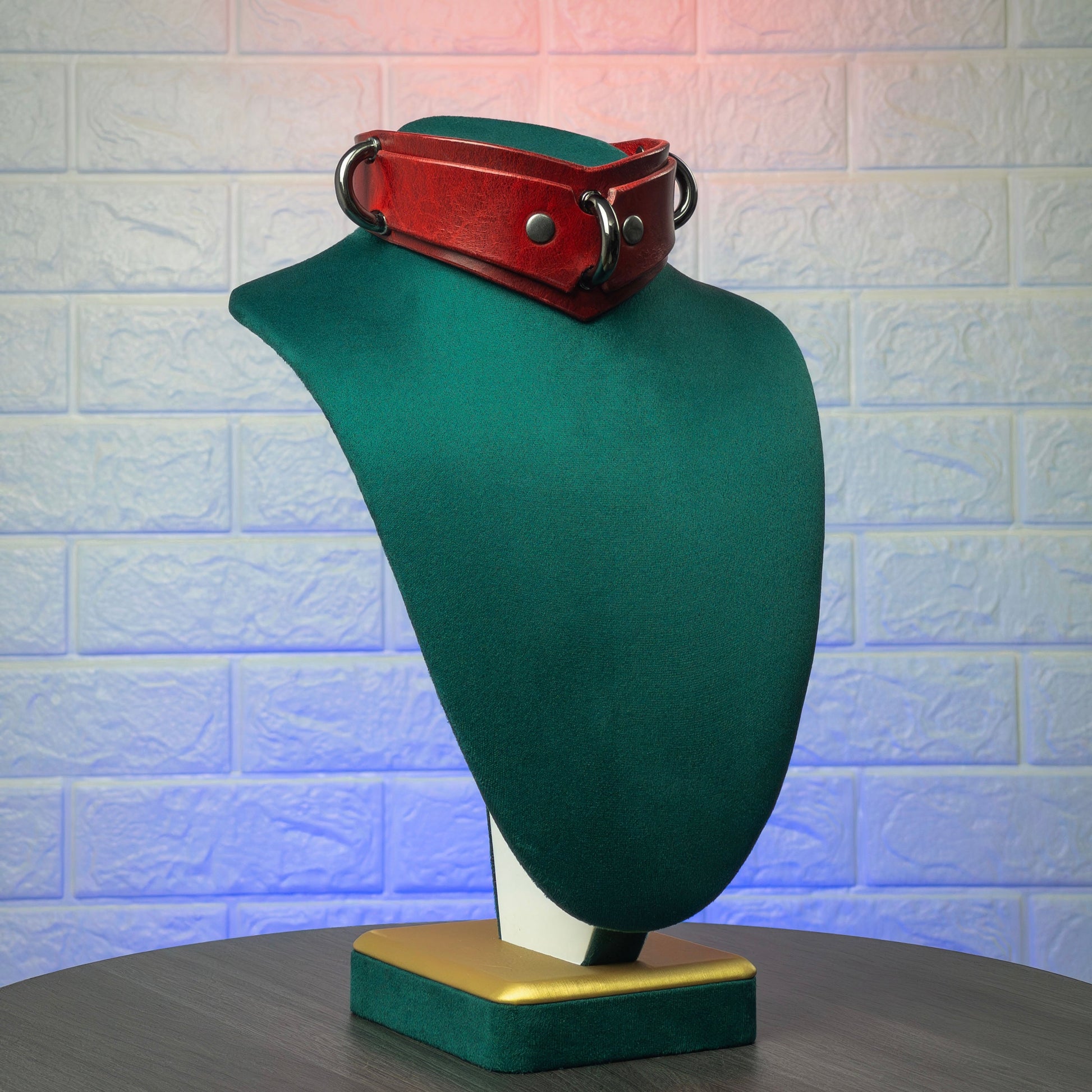 Red leather collar on a green mannequin against a textured white wall.