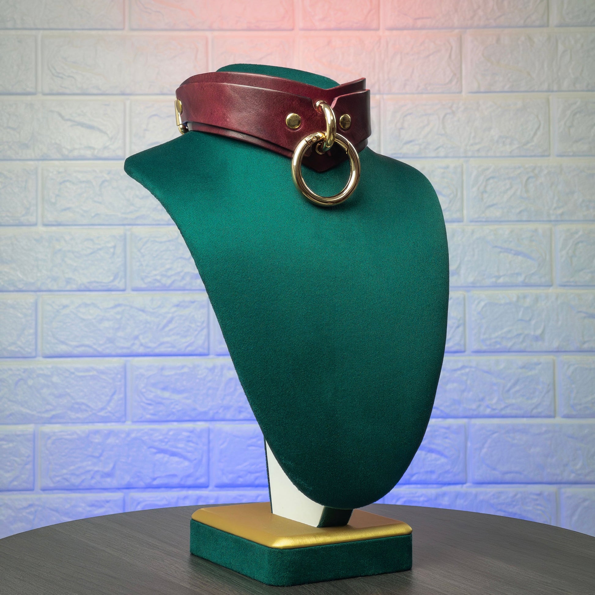 Marsala mannequin head with a brown leather belt and gold ring against a textured wall.