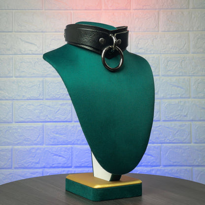 Black leather collar on a green mannequin bust against a textured wall background