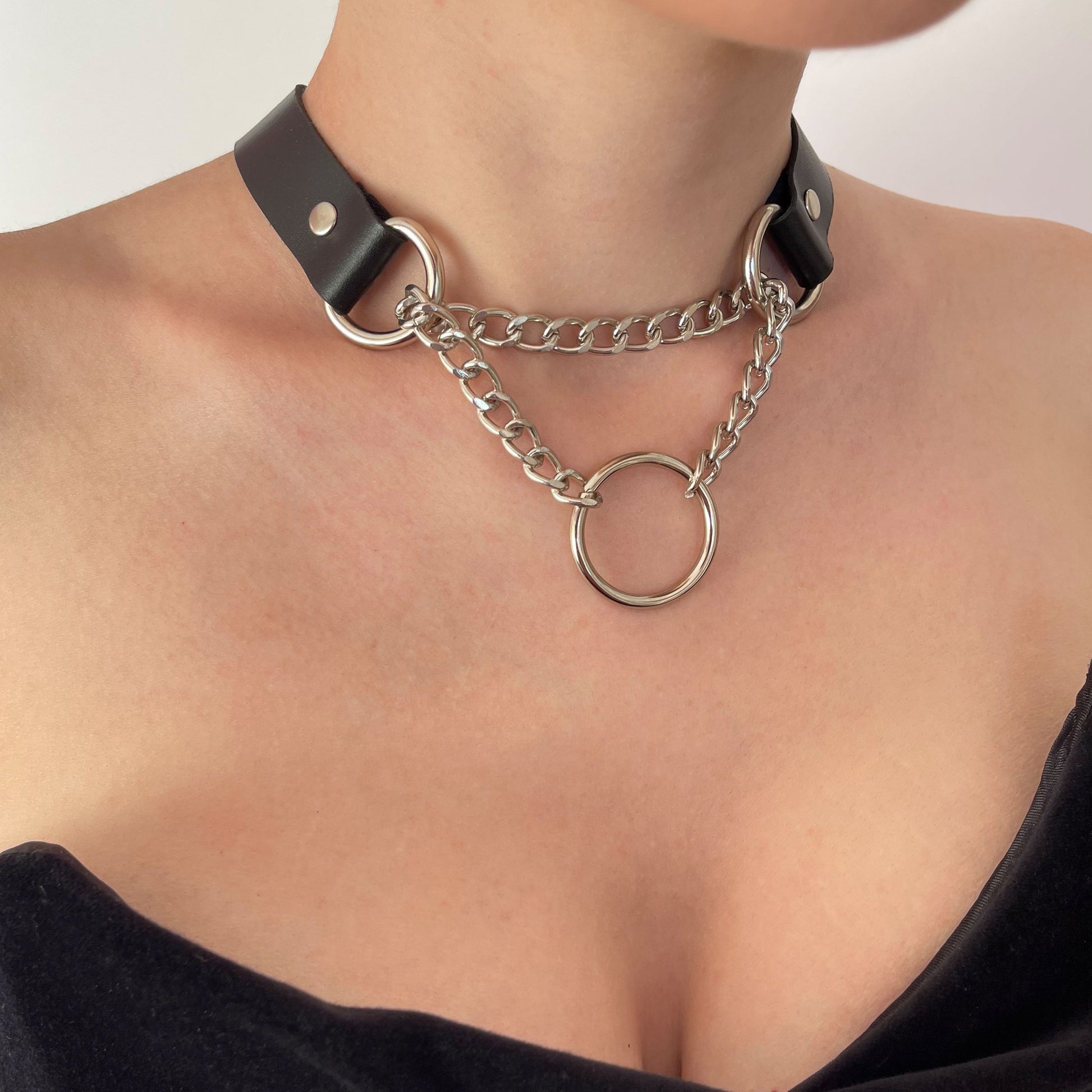 Black leather choker with silver hardware, O-ring, and layered chains. Styled with a black top.