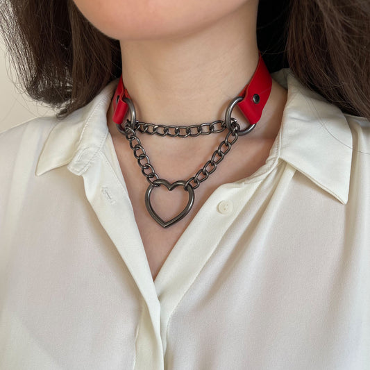 Red leather choker with dark metal heart-shaped hardware on model’s neck, side view