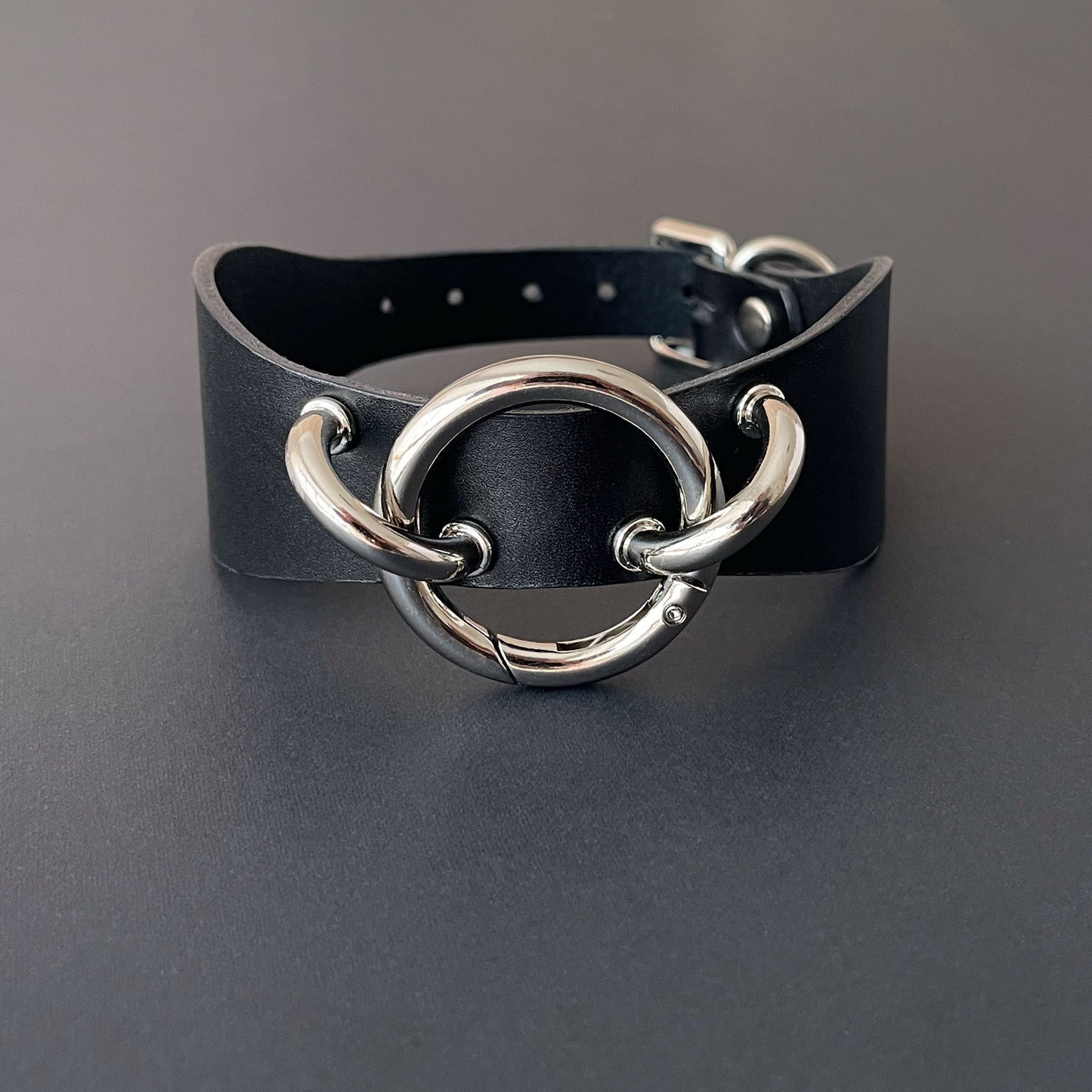 Black leather collar with silver metal rings on a gray background