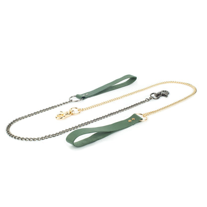 BDSM leather chain leash on a white background, green leather hand loop connected to a 60 cm metal chain with a carabiner fixed directly to the chain end. The photo shows the same leash with two hardware finishes, dark nickel and gold, laid flat side by side.