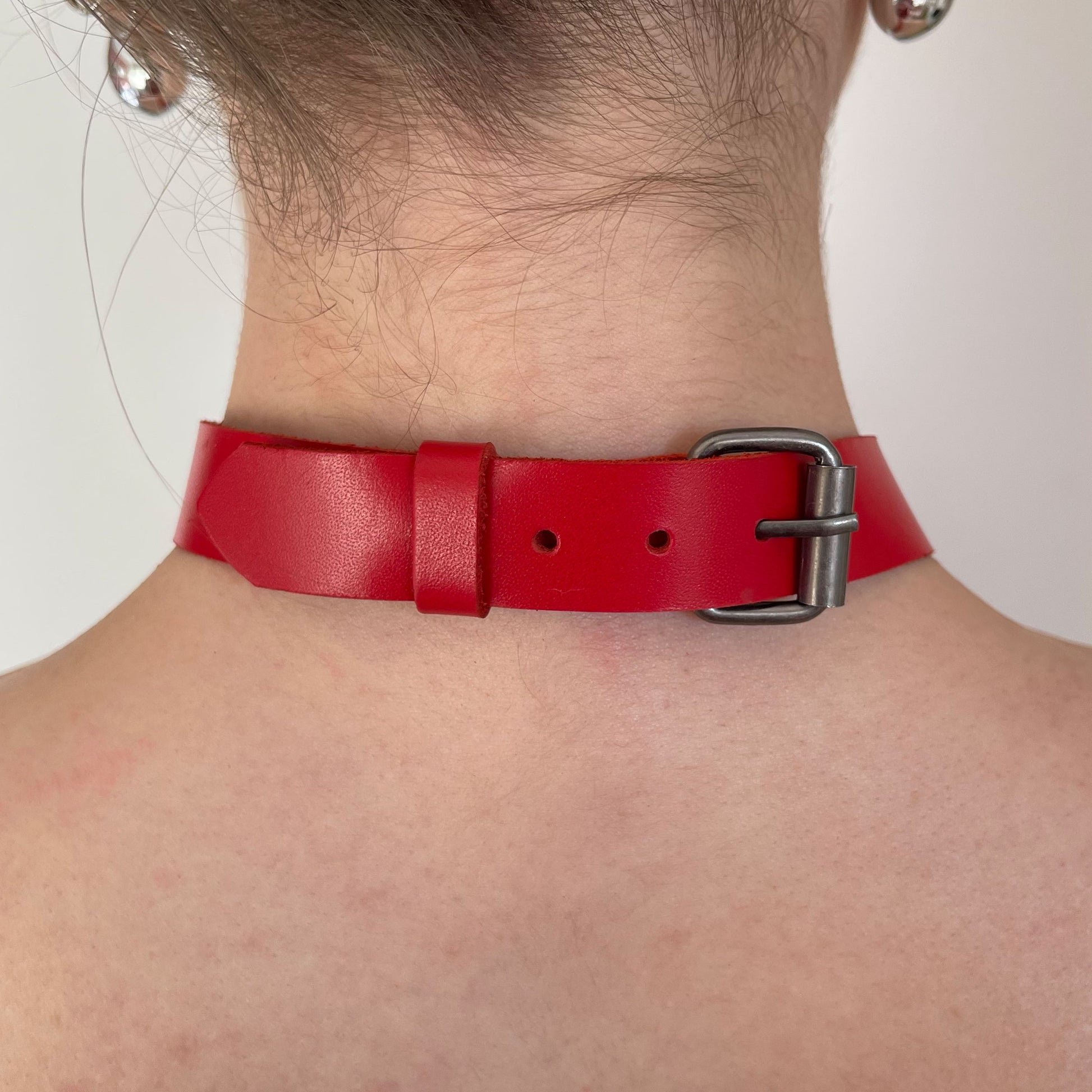 Back view of red leather choker with adjustable dark nickel buckle and smooth leather strap.
