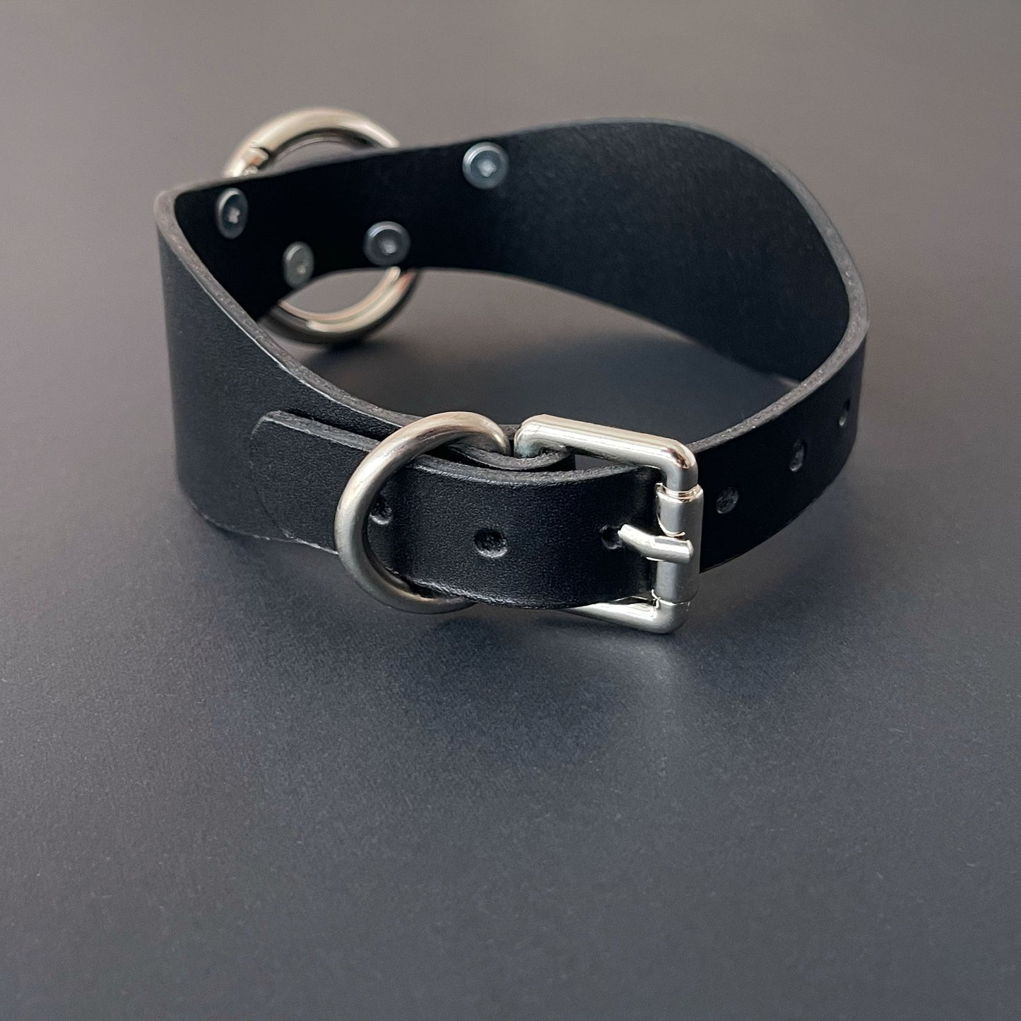 Black leather collar with silver hardware on a gray background