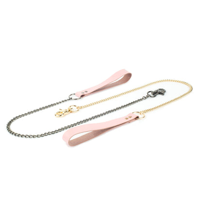 BDSM leather chain leash on a white background, pink leather hand loop connected to a 60 cm metal chain with a carabiner fixed directly to the chain end. The photo shows the same leash with two hardware finishes, dark nickel and gold, placed flat to compare hardware.
