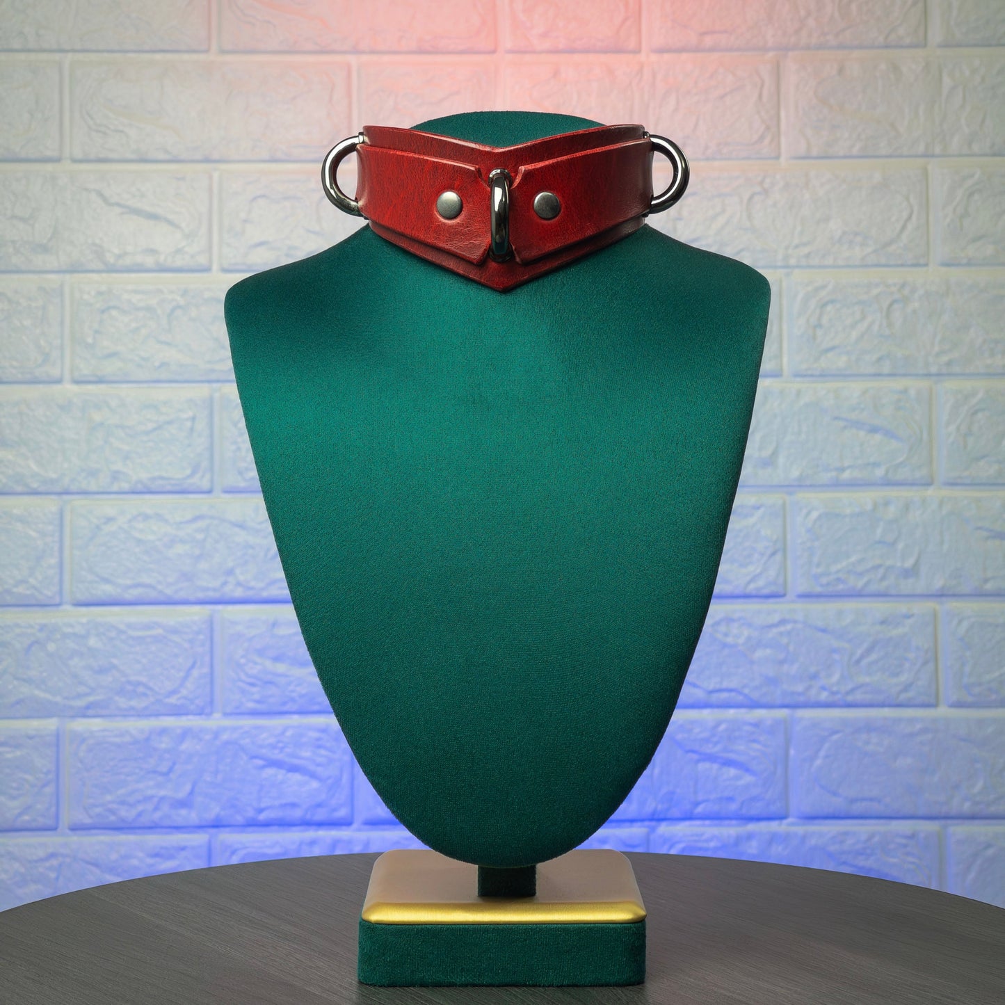 Red leather collar on a green mannequin bust against a textured white wall.