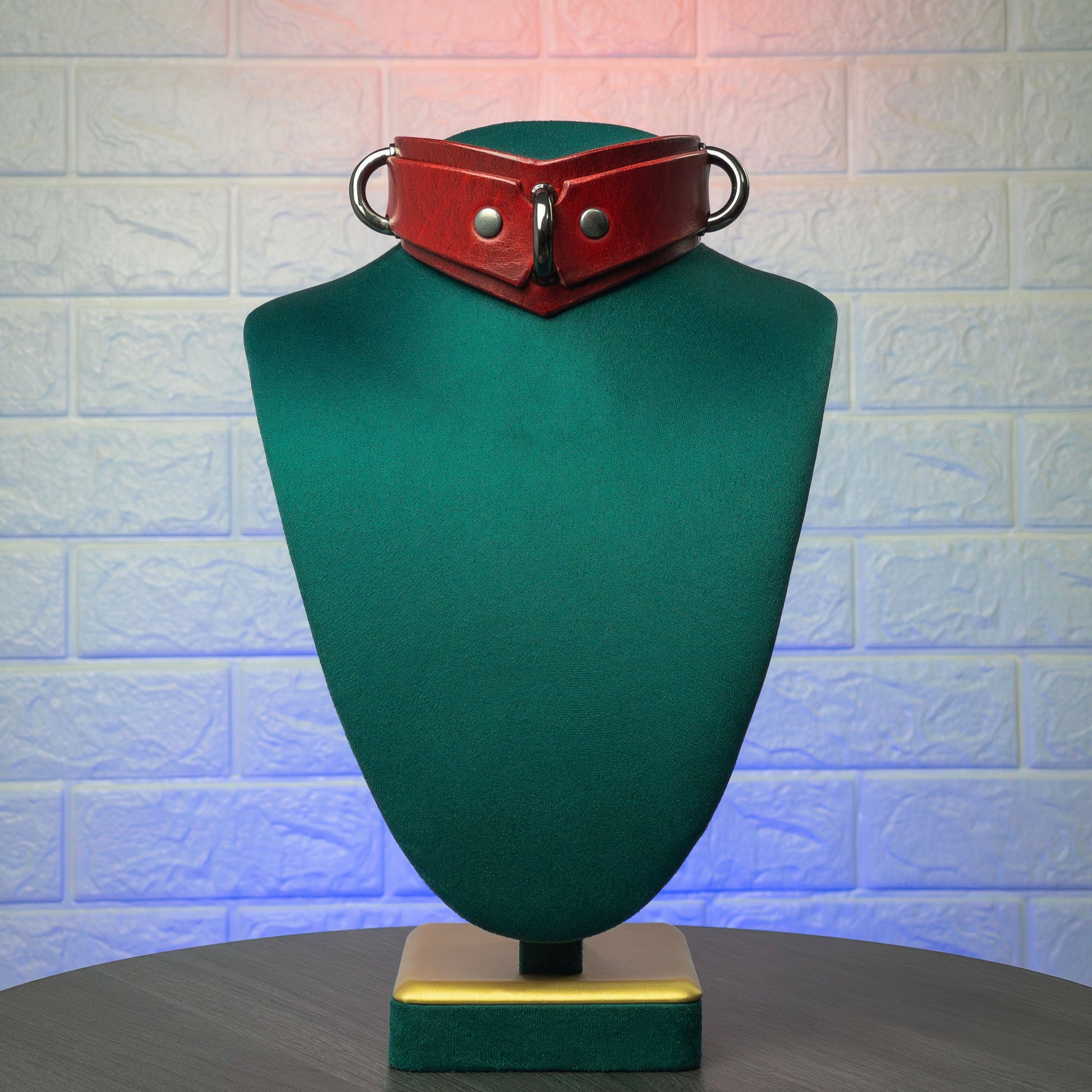 Red leather collar on a green mannequin bust against a textured white wall.