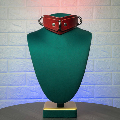 Red leather collar on a green mannequin bust against a textured white wall.