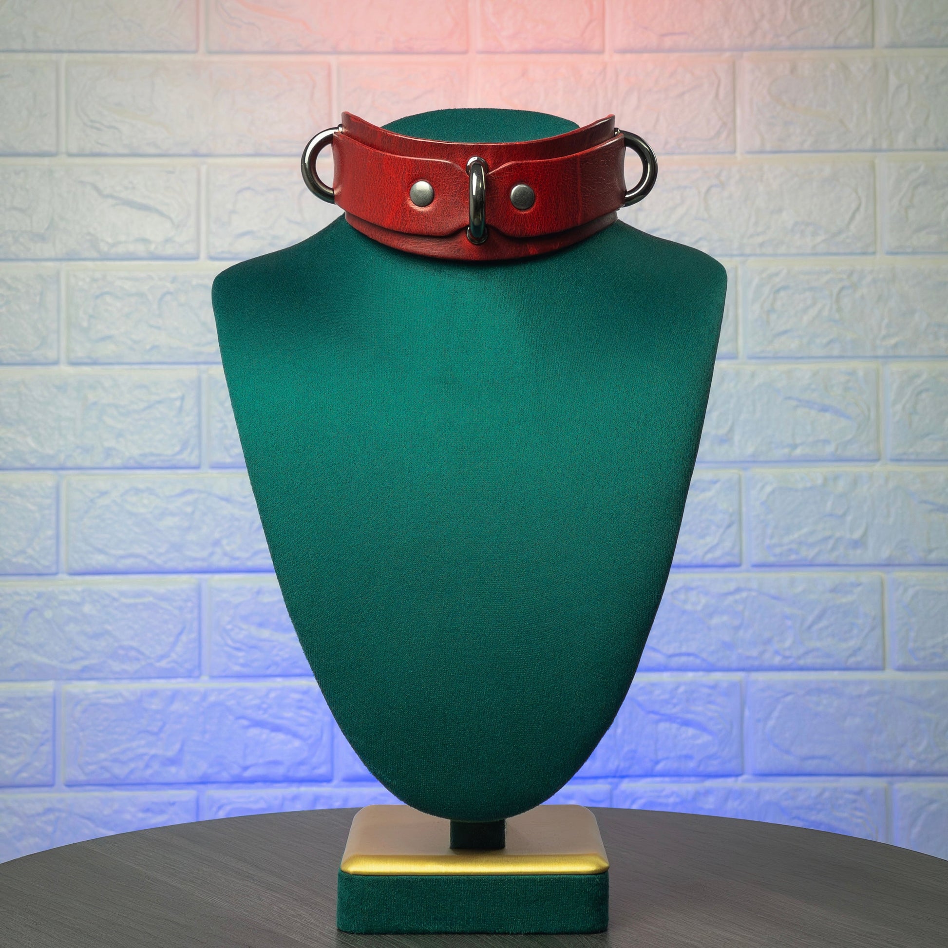 Red leather collar on a green mannequin bust against a textured white wall.