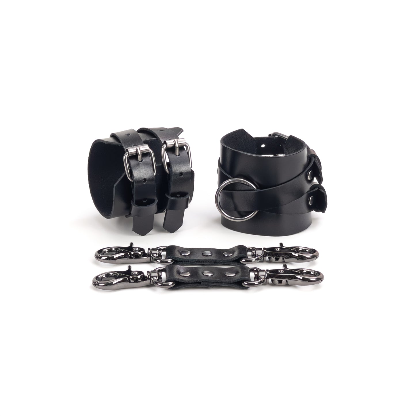 Leather handcuffs with crossed straps displayed on a white background, one cuff shown from the buckle side and the other from the side with a central round metal ring. Each handcuff has a 6 cm (2.36 in) wide leather base with crossed 15 mm (0.59 in) straps fixed to it, made from leather 1.4–1.8 mm (0.055–0.071 in) thick, with a leather connector placed in front.