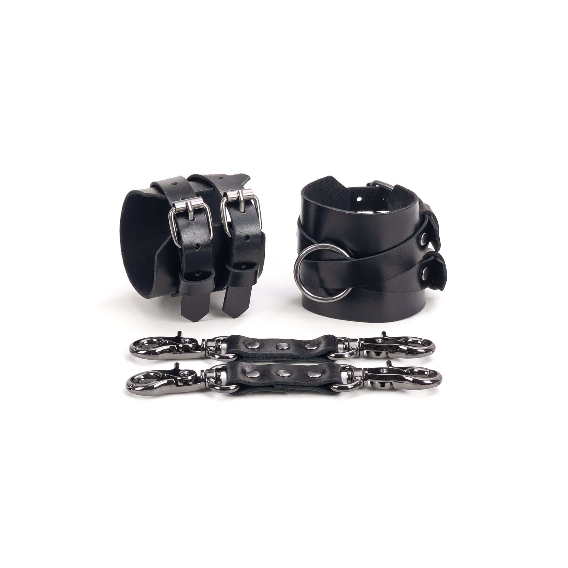 Leather handcuffs with crossed straps displayed on a white background, one cuff shown from the buckle side and the other from the side with a central round metal ring. Each handcuff has a 6 cm (2.36 in) wide leather base with crossed 15 mm (0.59 in) straps fixed to it, made from leather 1.4–1.8 mm (0.055–0.071 in) thick, with a leather connector placed in front.