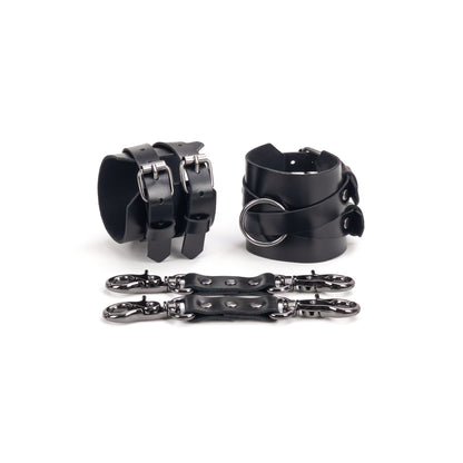 Leather handcuffs with crossed straps displayed on a white background, one cuff shown from the buckle side and the other from the side with a central round metal ring. Each handcuff has a 6 cm (2.36 in) wide leather base with crossed 15 mm (0.59 in) straps fixed to it, made from leather 1.4–1.8 mm (0.055–0.071 in) thick, with a leather connector placed in front.