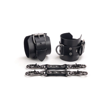 Close-up of black leather wrist cuffs with dark nickel hardware, with two leather connectors placed next to them, showing how the cuffs and connectors look together.