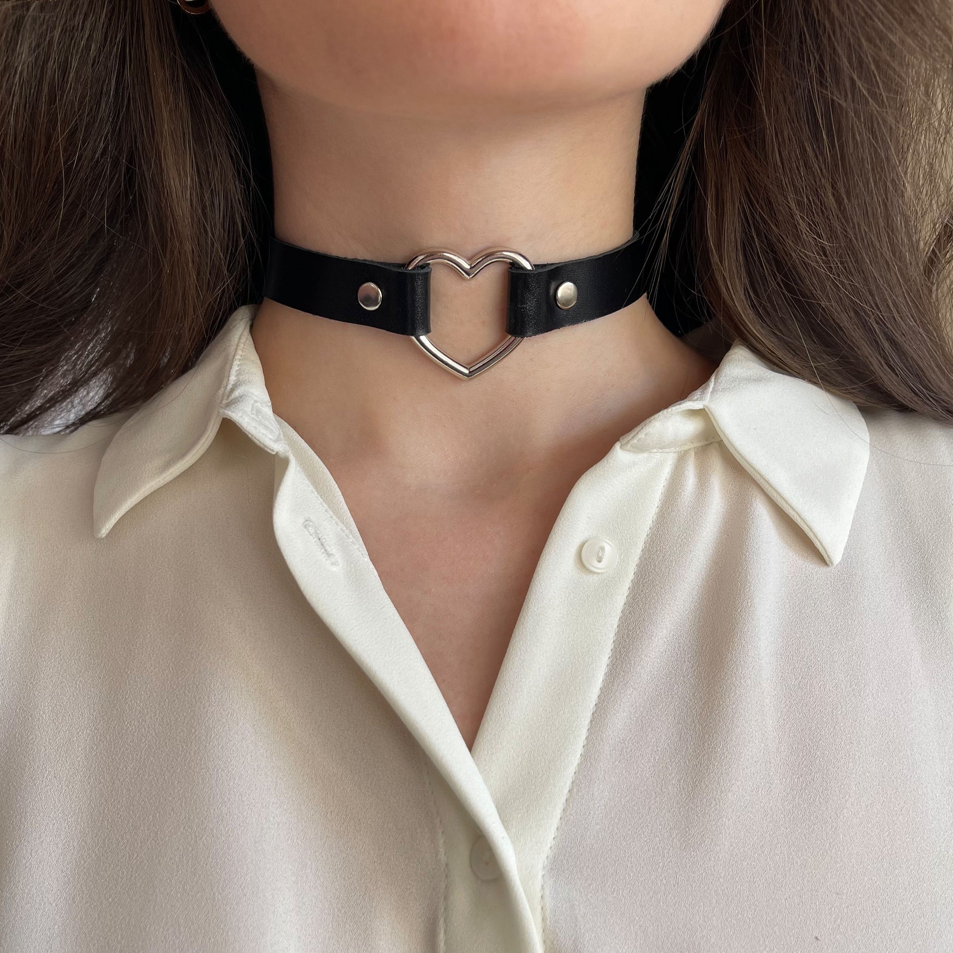 Black leather choker with silver heart-shaped ring – centered front view on model wearing ivory shirt