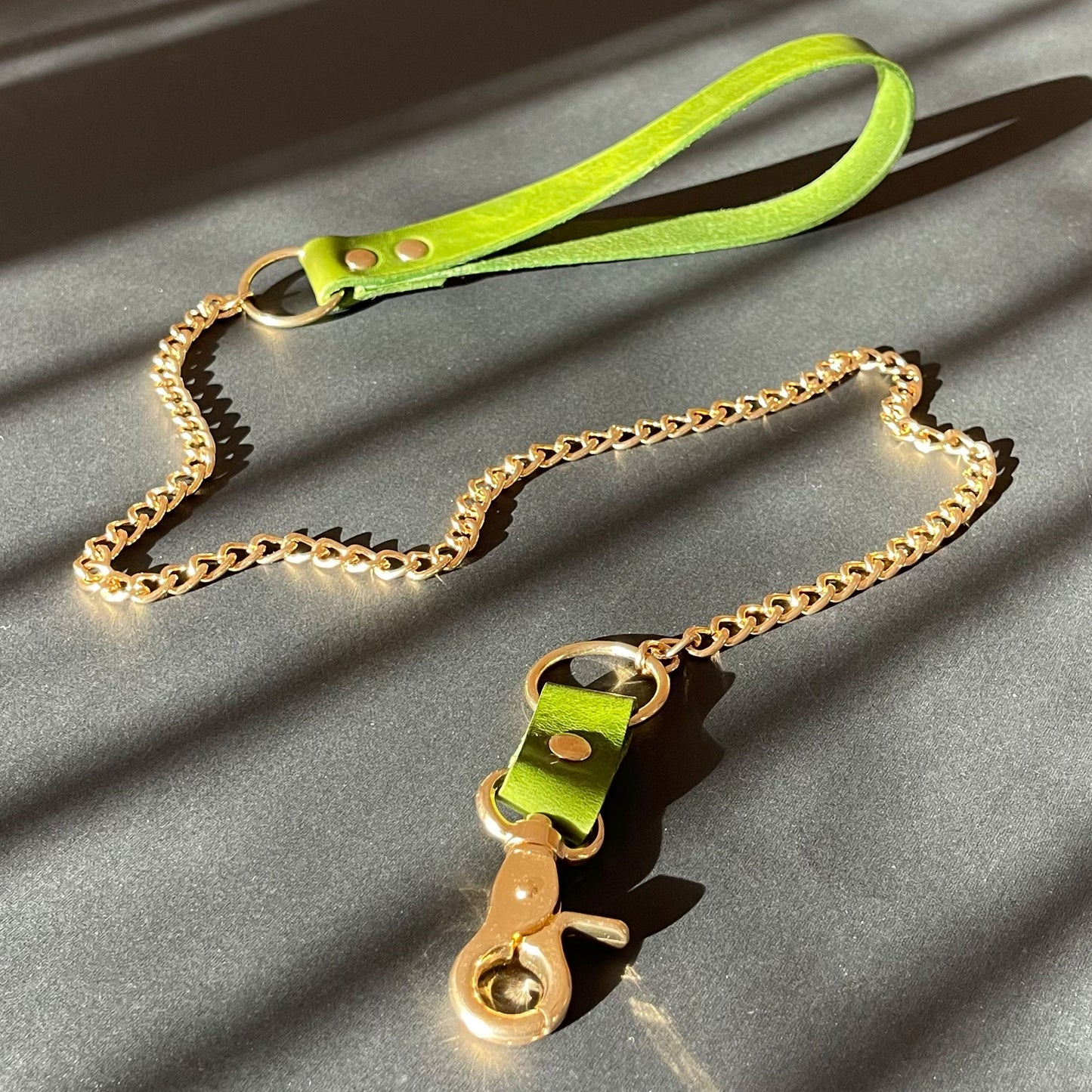 Green leather bondage leash with gold chain on a gray surface