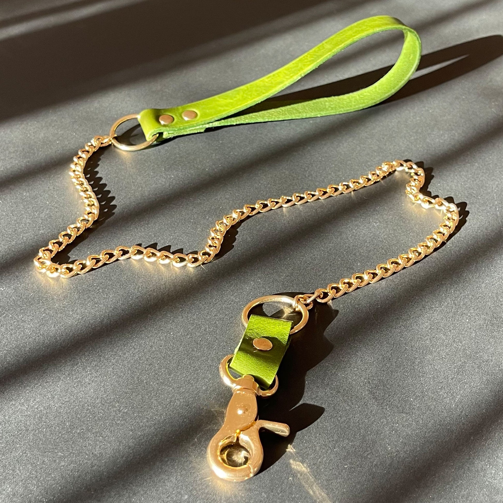 Green leather bondage leash with gold chain on a gray surface