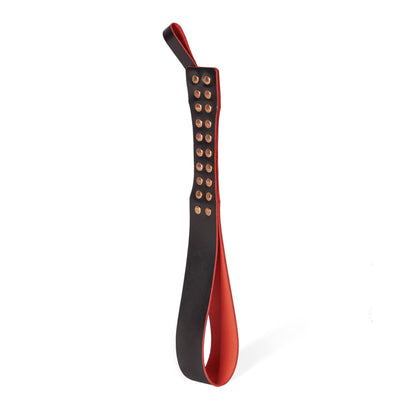 Handmade leather Loop Core BDSM paddle photographed upright on a white background. Crafted from a single piece of thick belt leather folded into a distinctive loop construction with decorative metal studs and a narrow striking surface for bondage and impact play.