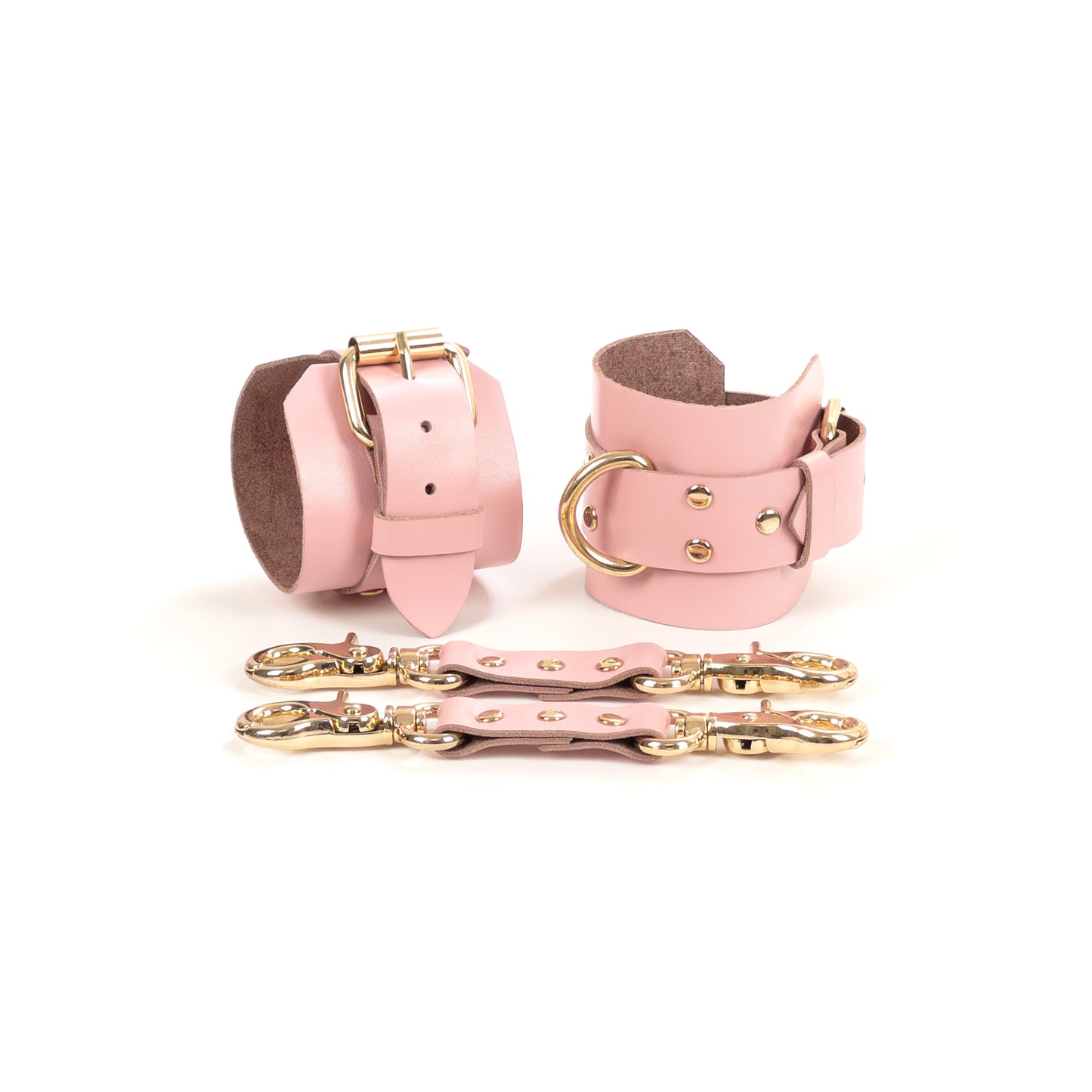 Pink leather handcuffs with gold-tone hardware shown on a white background, made from leather 1.4–1.8 mm (0.055–0.071 in) thick, featuring a 6 cm (2.36 in) wide base, 2.5 cm (0.98 in) adjustable straps, and 2.5 cm (0.98 in) D-rings, with leather connectors placed in front.