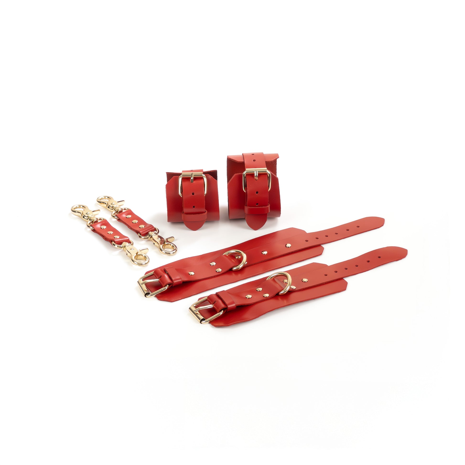 Red leather BDSM set laid flat: wrist cuffs and ankle cuffs with buckle straps, rivets, adjustment holes, and gold-tone hardware. Each cuff has a 2.5 cm D-ring. Two matching leather connectors with gold-tone carabiners on both ends are placed next to the cuffs.
